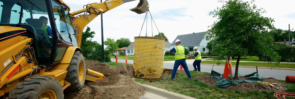 A Bob Frame Plumbing backhoe lowering a safety box into a street excavation