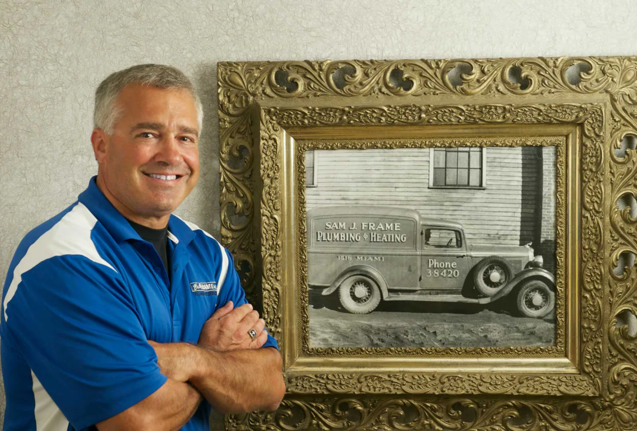 Dave Frame beside a framed photograph of an early Sam J. Frame Plumbing & Heating truck
